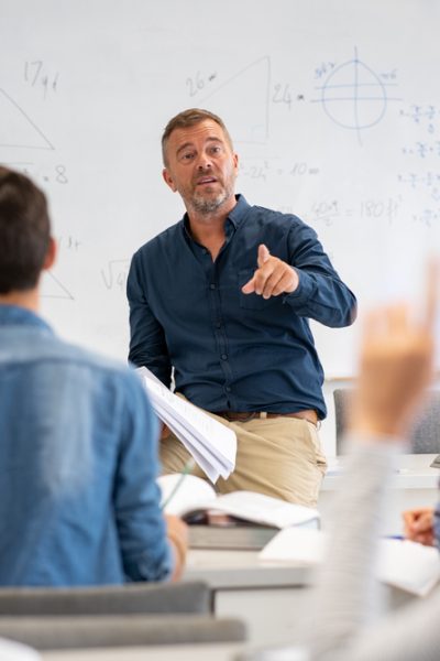 Professor,Pointing,At,College,Student,With,Hand,Raised,In,Classroom.